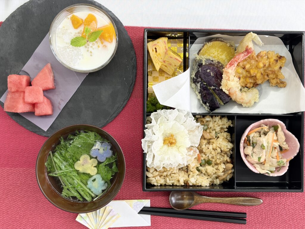 炊き込みご飯や天ぷら、すいか、ミルクデザートが並んだお祝いのお弁当